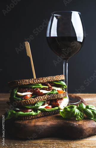 Homemade caprese sandwich and glass of red wine on wooden board  dark background  selective focus  vertical composition