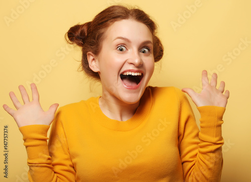 Beautiful young surprised redhair woman over yellow background