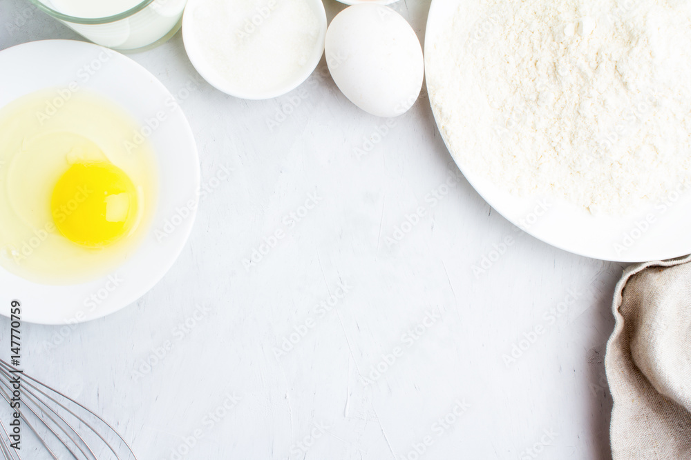 Flour, eggs, sugar, milk, rolling pin and whisk on a white background close-up. Flour, eggs, sugar, milk, rolling pin and whisk on a white background close-up.
