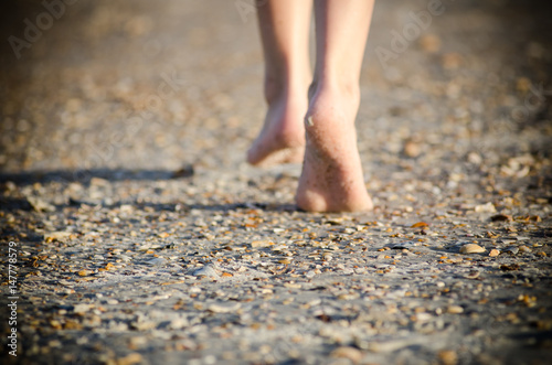 Young child walking barefoot on sandy beach with shells