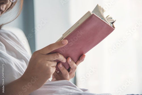 Asian woman reading a book on her bed.