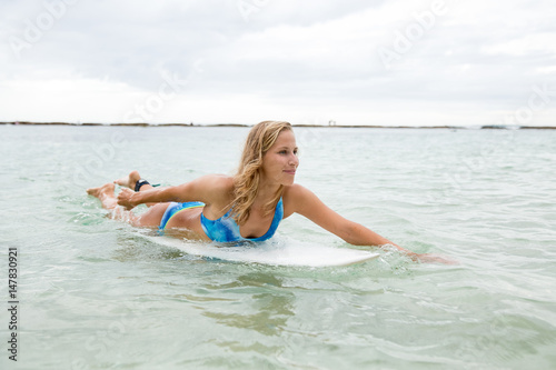 Smiling Woman Lying on Surfboard and Rowing in Sea © Mangostar