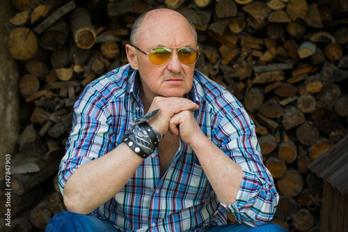 Portrait bold man is an American near the wood and firewood in a plaid shirt, stylish appearance with mans accessories photo