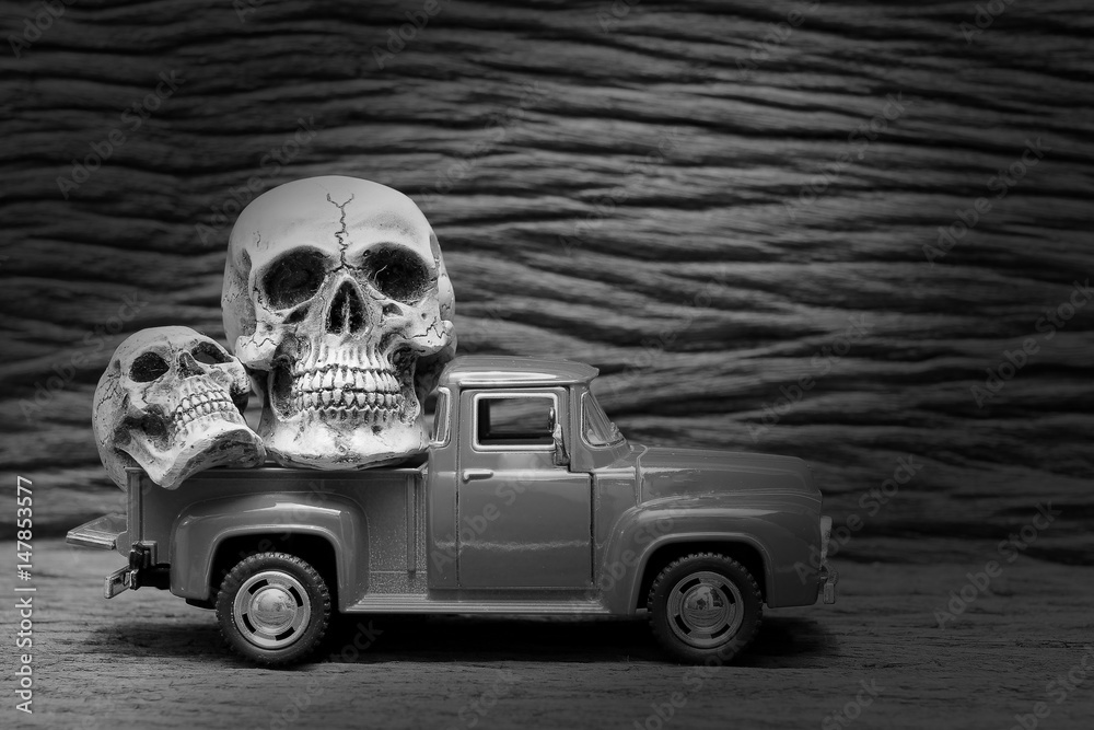 black and white shot of Still life painting photography with human skull on vintage image of pickup truck toy on wooden background.