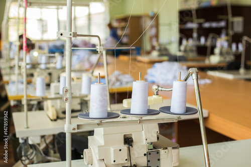 Closeup of three big bobbins with thin white thread on working professional sewing machine.  Horizontal color photo.