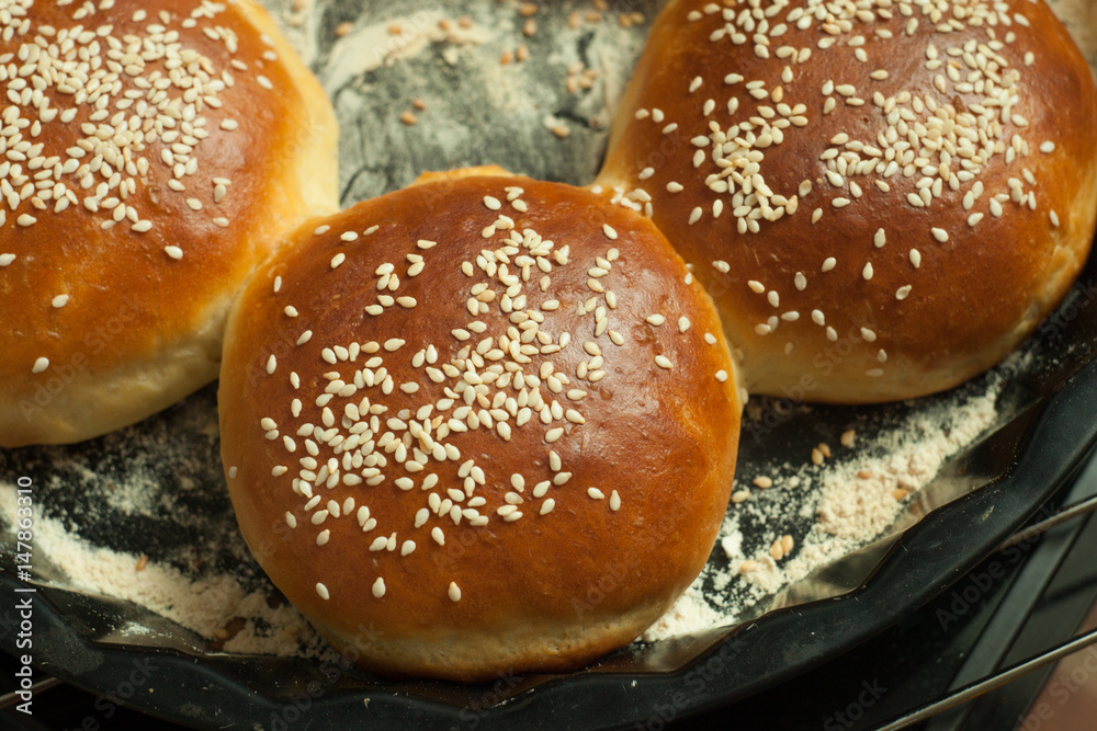 buns for burgers with sesame in a baking form on black background, top view 2