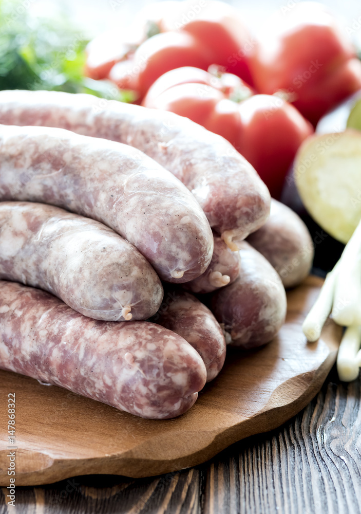 Raw sausages lying on wooden board Fresh vegetables and greens Vertical photo Raw sausages lying on wooden board Fresh vegetables and greens Vertical photo