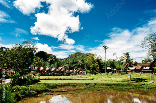 Traditional Tana Toraja village  tongkonan houses and buildings. Sunny  blue sky with clouds  lake in a foreground. Kete Kesu  Rantepao  Sulawesi  Indonesia