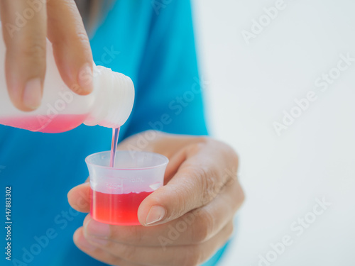 healthcare, people and medicine concept - woman pouring medication or antipyretic syrup from bottle to cup