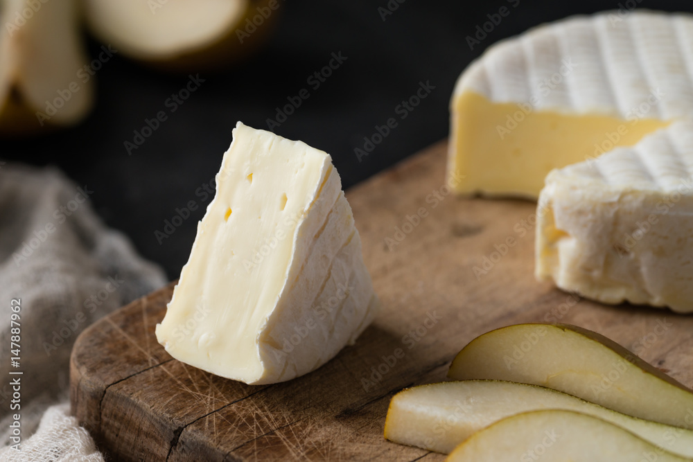 Closeup of French soft cheese from Normandy region sliced with pear on a wooden board on dark rustic background