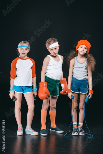Three active kids in sportswear posing with sport equipment isolated on black