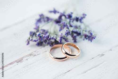 Tablou pe pânză Close-up view of golden wedding rings and beautiful small blue flowers on wooden