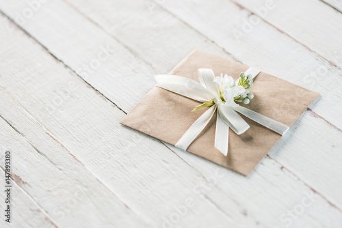 envelope with flower and ribbon on white wooden tabletop, invitation card wedding concept