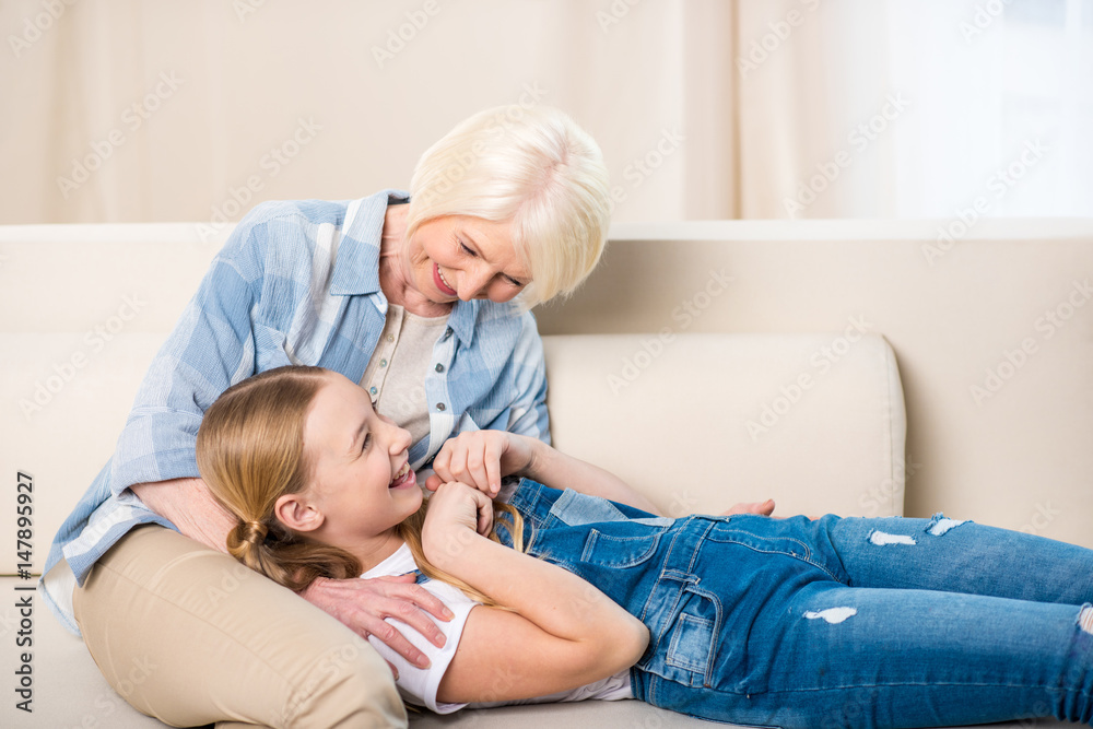 Happy grandmother and granddaughter having fun together on sofa