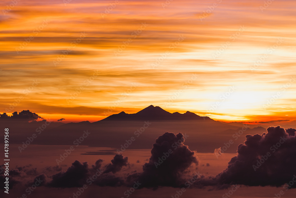 View of Rinjani peak from top of Agung volcano in Bali at sunrise summit. Sunrays and colorful sky, panoramic landscape, Agung trekking