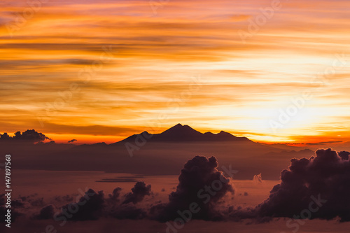 View of Rinjani peak from top of Agung volcano in Bali at sunrise summit. Sunrays and colorful sky  panoramic landscape  Agung trekking