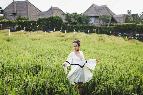 Young woman in white tunic in rice fields Bali in Tegallalang. Rustic Ubud village landscape outside. Fashion style, curly hair, light dress photo