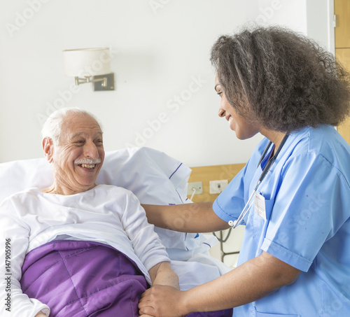 Reassuring confident african female doctor visiting elderly caucasian patient in hospital bed