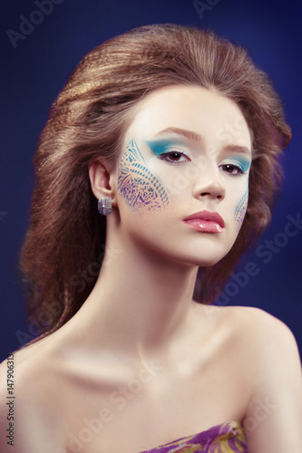 Fashion beauty portrait of a beautiful girl with creative make-up with patterns on a blue background.
