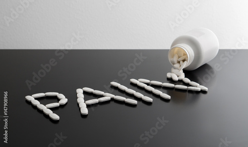 Pain killers spilling from bottle on table. Being in a lot of pain, suffering or relief concept. The word pain written with medicine coming out from package. Writing made with medical products. 
