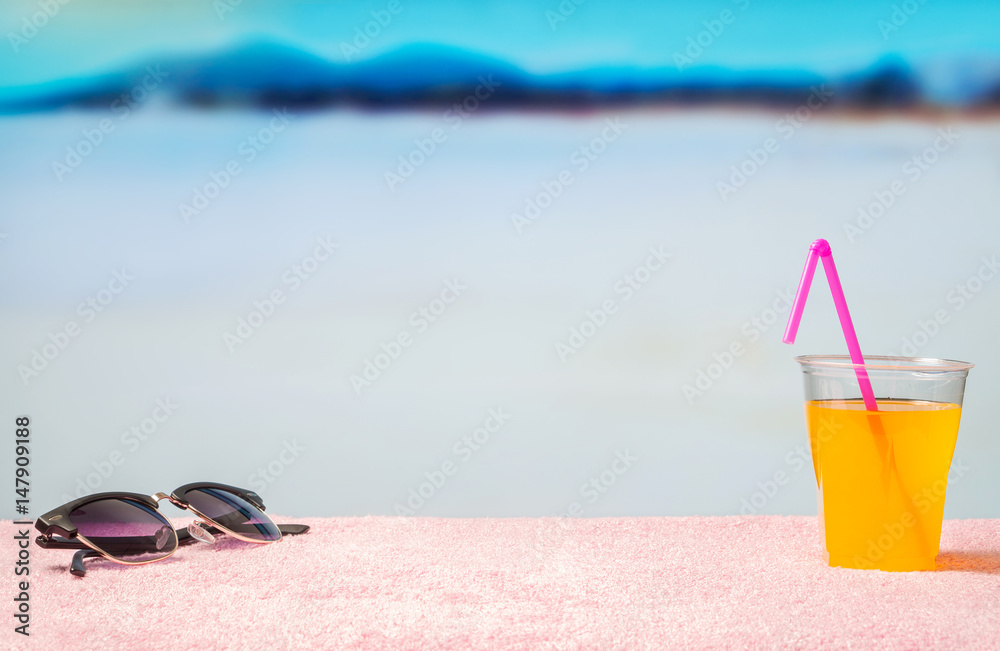 Vacation background with free blank copy space. Sunglasses and yellow cocktail with pink straw on beach. Beautiful lagoon beach paradise in blurred in the back. Perfect template for summer designs.