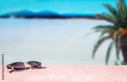 Beach background with free empty blank copy space. Trendy sunglasses on towel in beautiful paradise. Perfect lagoon beach and a palm tree in the blurred back. Clear sky and hot summer atmosphere.