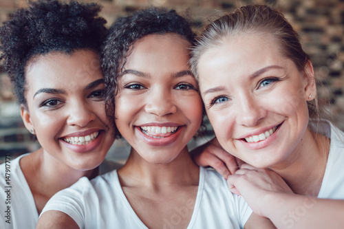 Beautiful and funny girls in white T-shirts makes selfie. Two afro-americans and one european.