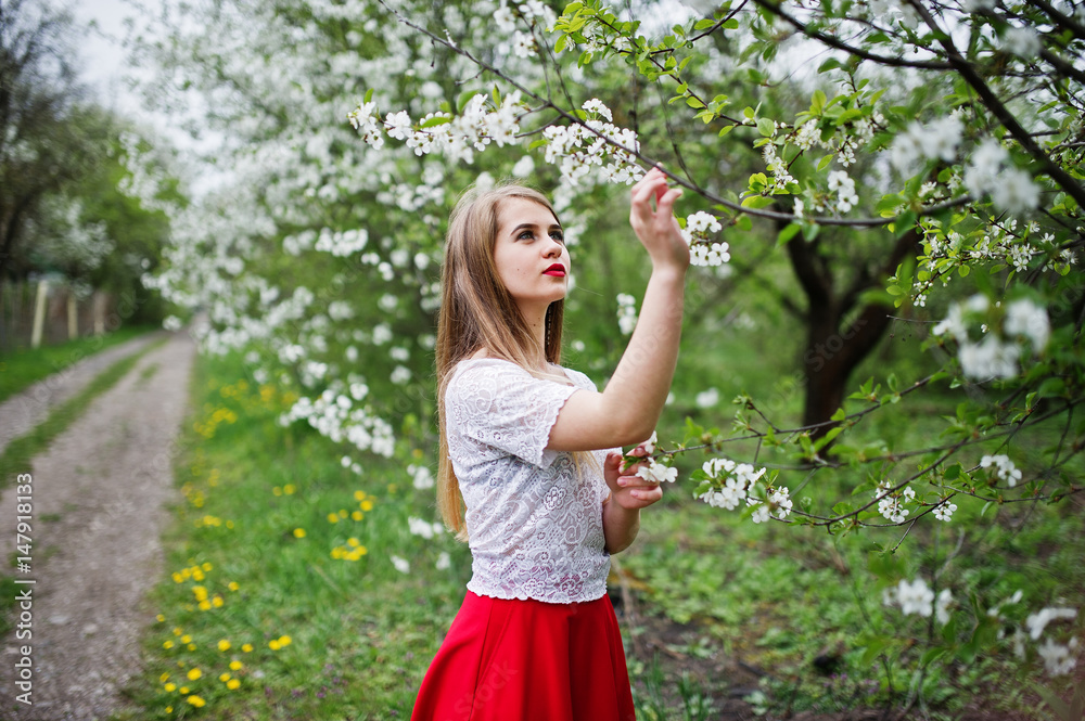 Portrait of beautiful girl with red lips at spring blossom garden, wear on red dress and white blouse.