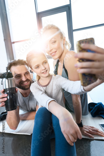 Girl taking self portrait with parents at fitness center