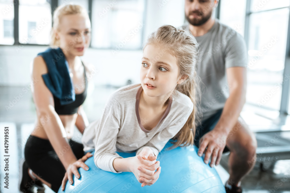 Cute gir exercising on swiss ball with parents