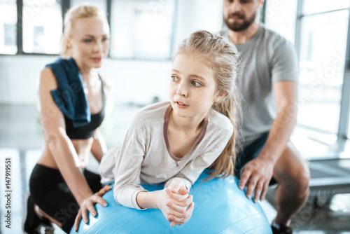 Cute gir exercising on swiss ball with parents