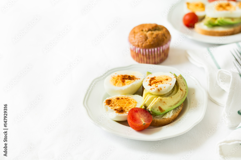 Healthy breakfast: toasts with avocado slices, tomato, paprika and eggs on white tableware. Selective focus