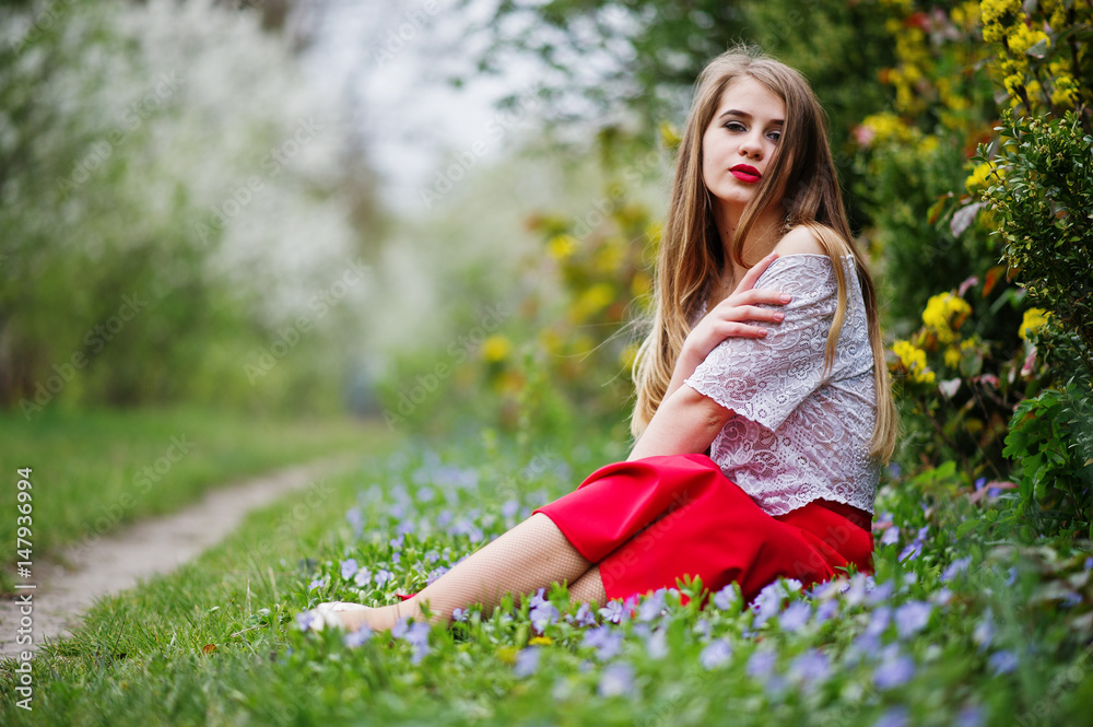 Portrait of sitiing beautiful girl with red lips at spring blossom garden on grass with flowers, wear on red dress and white blouse. Portrait of sitiing beautiful girl with red lips at spring blossom garden on grass with flowers, wear on red dress and white blouse.