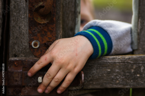 Sad Boy looking at a small window in a fence