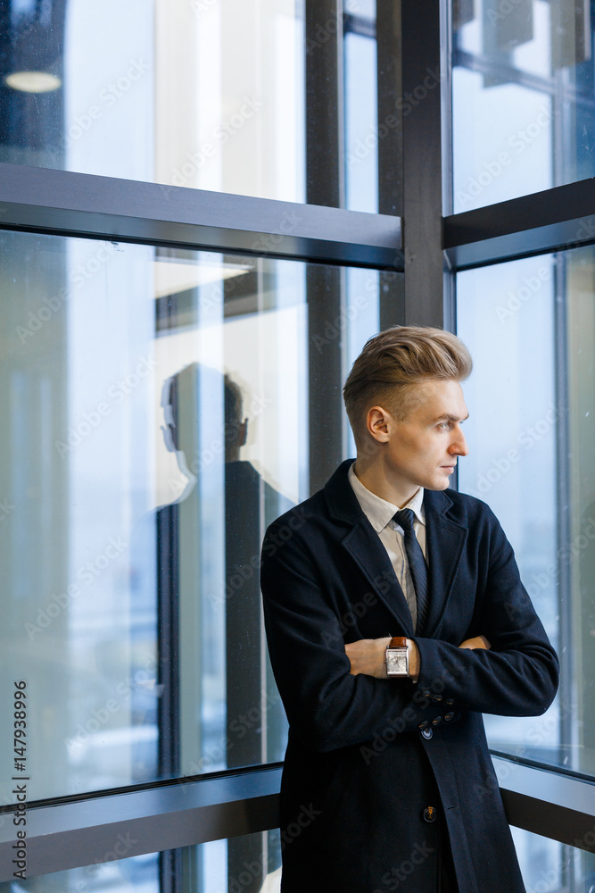 Thoughtful businessman wearing suit looking out window while standing with arms crossed in office corridor, waist-up portrait Thoughtful businessman wearing suit looking out window while standing with arms crossed in office corridor, waist-up portrait
