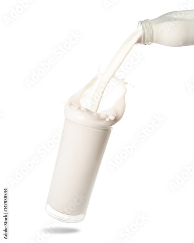 Pouring milk from bottle into glass with splashing on white background.