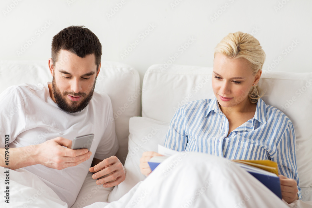 couple with book and smartphones in bed at home couple with book and smartphones in bed at home