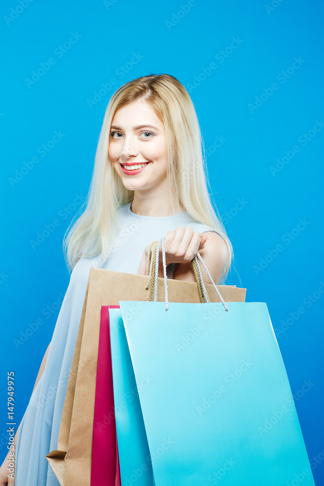 Pretty Woman Holding a Lot of Shopping Colorful Bags. Portrait of Cute Blonde with Long Hair on Blue Background.
