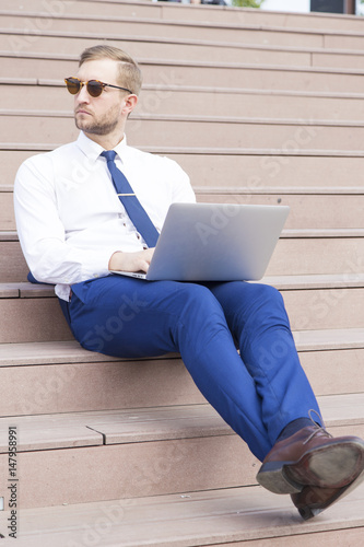 Handsome young businessman working on laptop sitting on the stairs outdoor