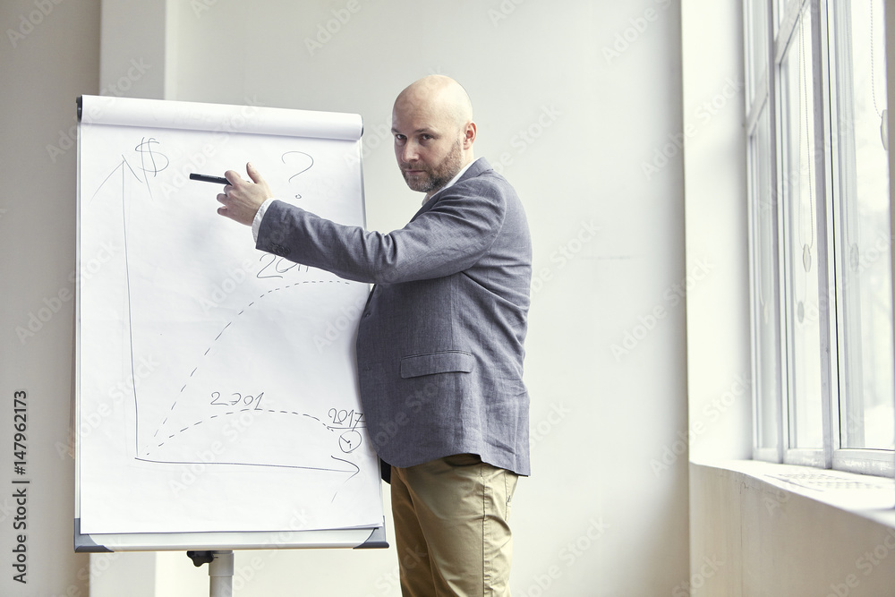 Bald Businessman Pointing at Something With a Marker