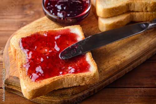 Toast with cherry jam on rustic wooden cutting board.