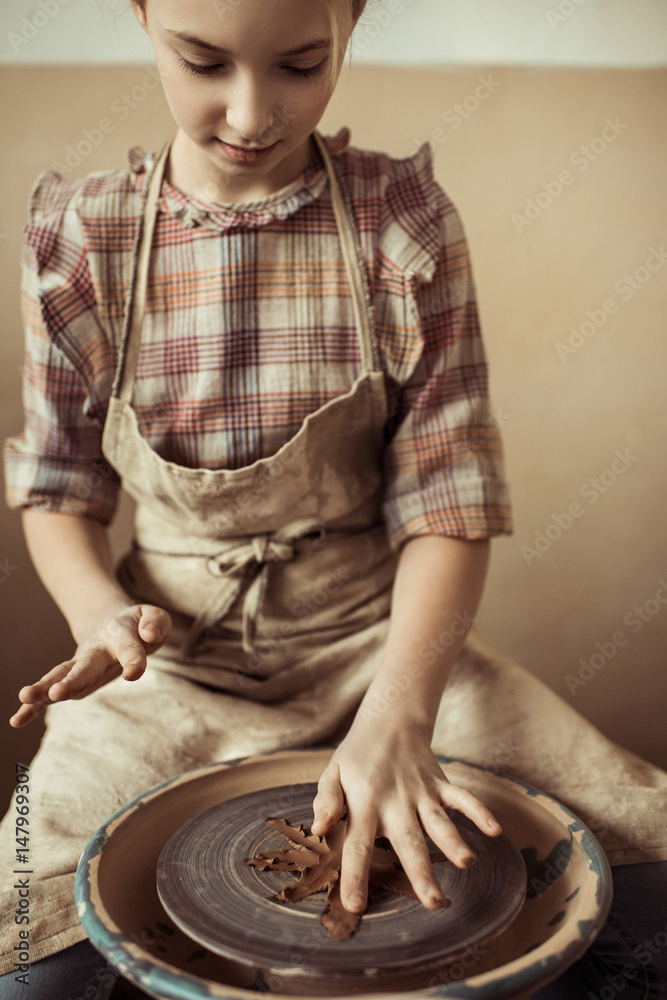 Front view of little girl making pottery on wheel at workshop