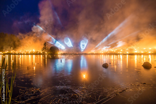 Light tubes on a horizon with a forest fire over a lake