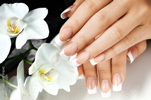 Valokuva Female hands with white nails on background of white flowers.