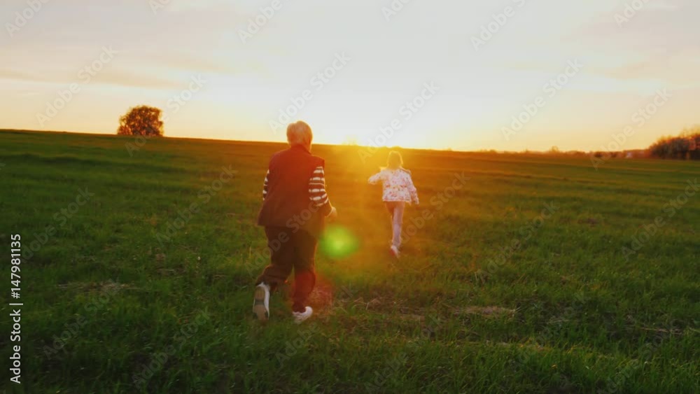 Active elderly people. Senior woman is running around with her granddaughter over a green meadow, playing dogganiks. On the Sunset. Concept - a healthy lifestyle, active old age