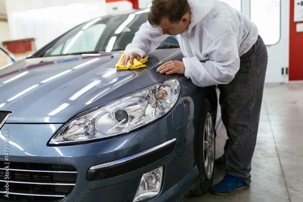 A man cleaning car with microfiber cloth, car detailing (or valeting) concept. Front lights protected with isolation blue tape. Selective focus. A man cleaning car with microfiber cloth, car detailing (or valeting) concept. Front lights protected with isolation blue tape. Selective focus.