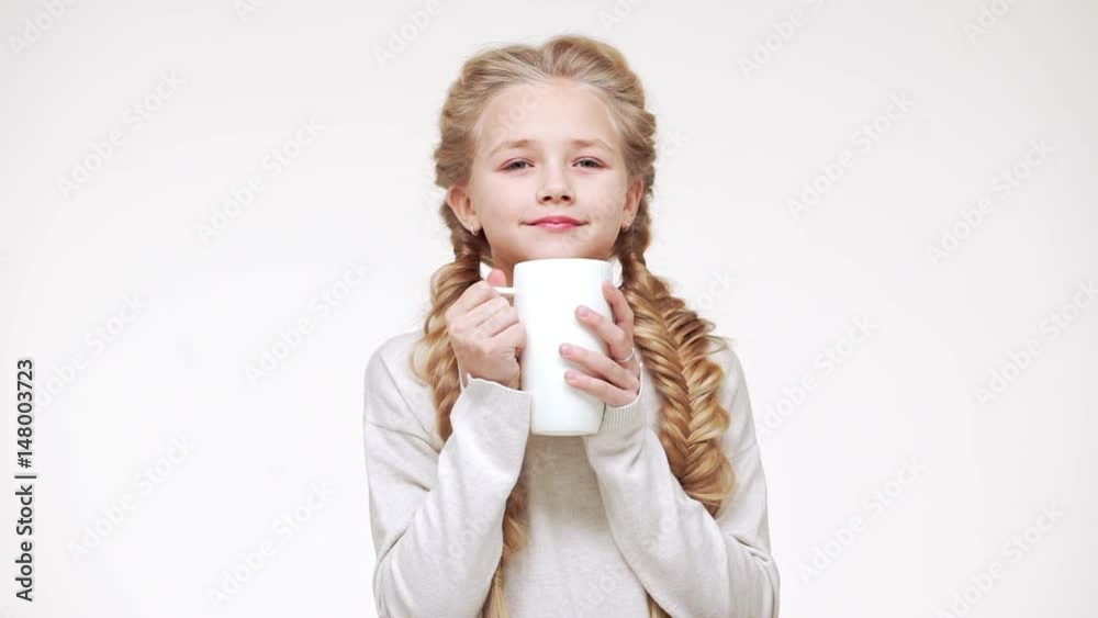 Small Caucasian beautiful Caucasian girl with luxurious long blonde hair drinking hot milk from cup and smiling in slowmotion Small Caucasian beautiful Caucasian girl with luxurious long blonde hair drinking hot milk from cup and smiling in slowmotion