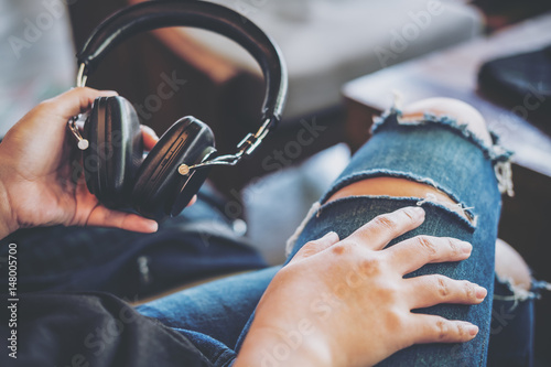 A woman wearing ripped jean   holding headphone and sitting in modern cafe with feeling relax