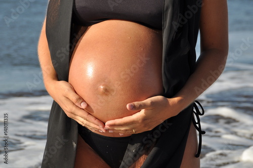 Mujer embarazada en la playa con manos en la barriga  photo