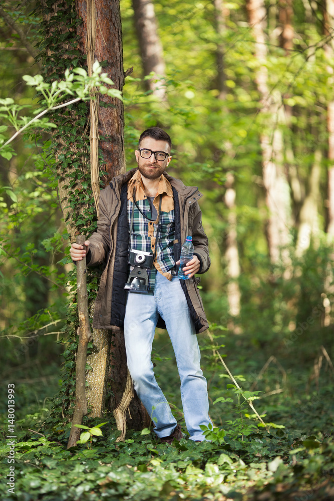 Young man is leaning on a tree while hiking in the woods